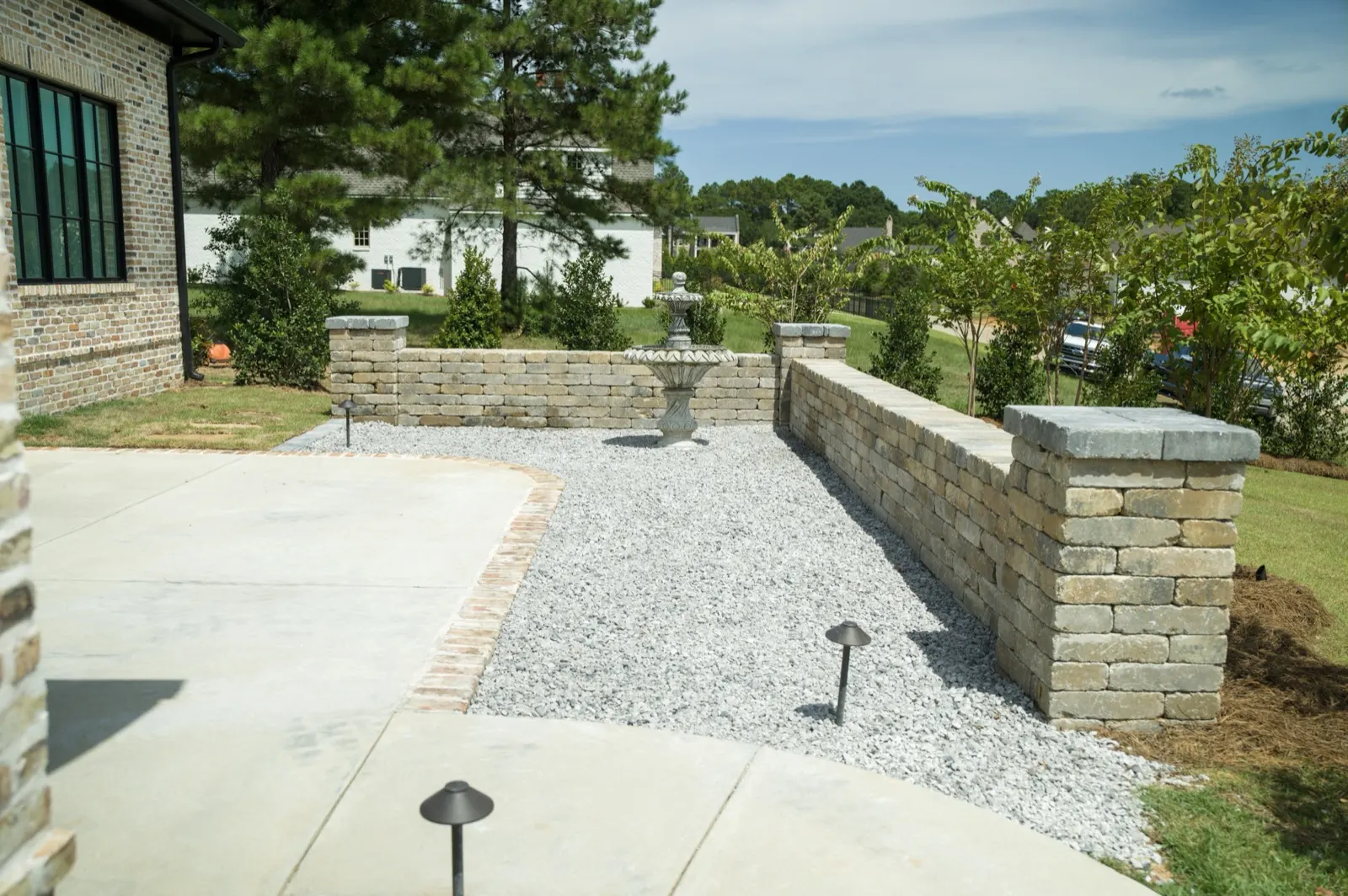 Concrete patio, low stone walls with capped pillars and a gravel court with a fountain at a home in Fairhope, Alabama