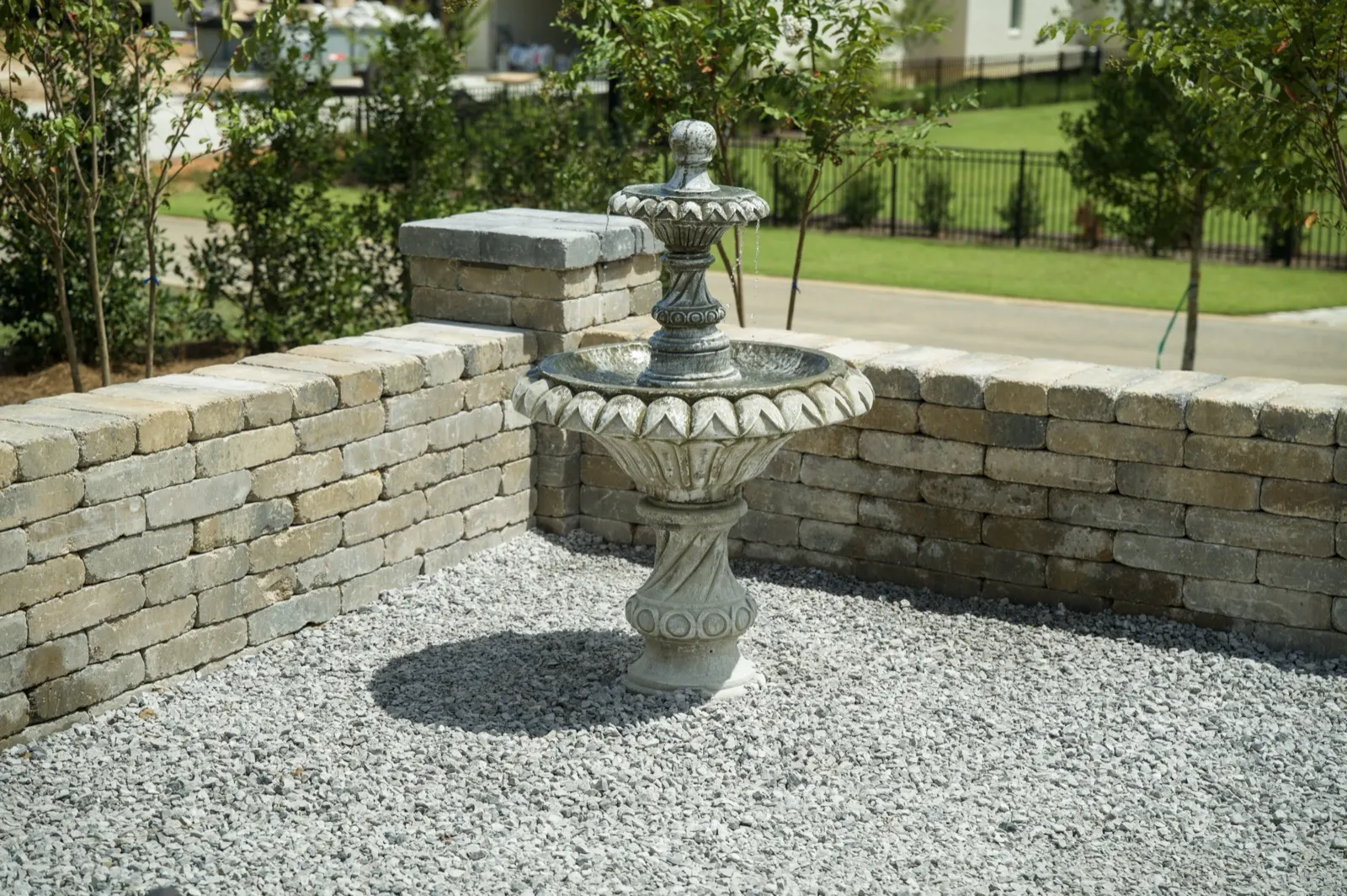 Tiered stone fountain on a white gravel bed inside a low stone seat wall at a Fairhope, Alabama home