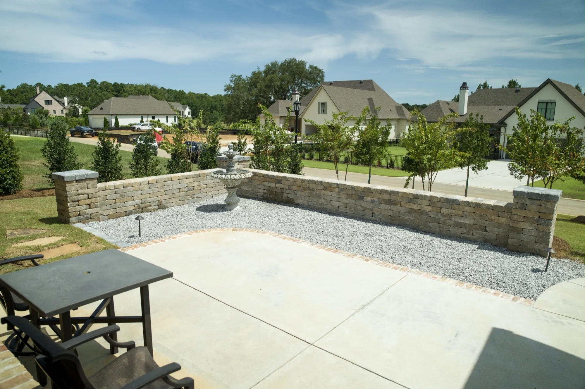 Concrete courtyard patio with a brick-edged border, low stone seat wall and a tiered fountain on white gravel at a Fairhope, Alabama home
