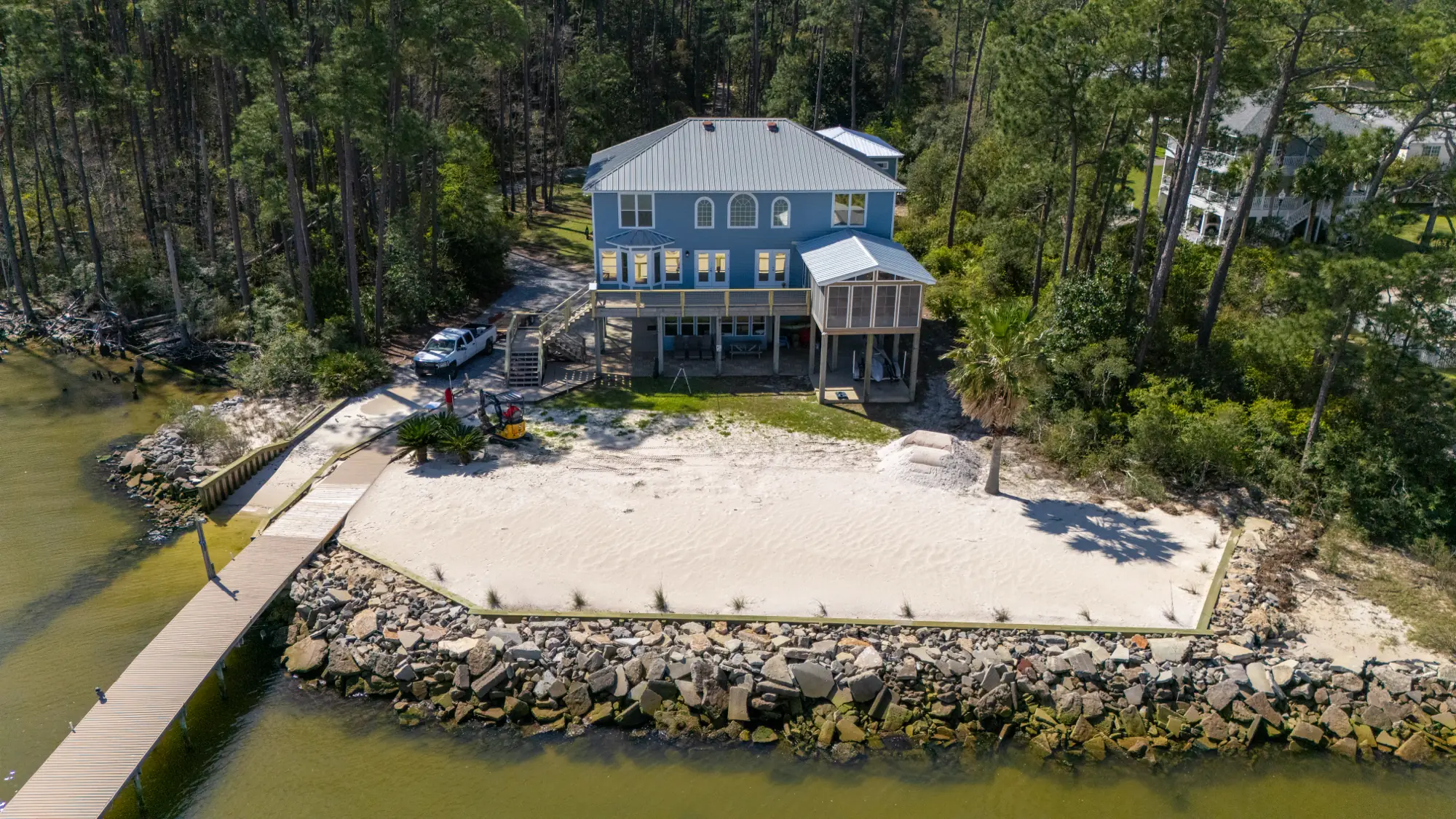 Aerial view of a bay-front property off Fort Morgan Road in Gulf Shores, Alabama, with a sand beach, rock seawall and pier