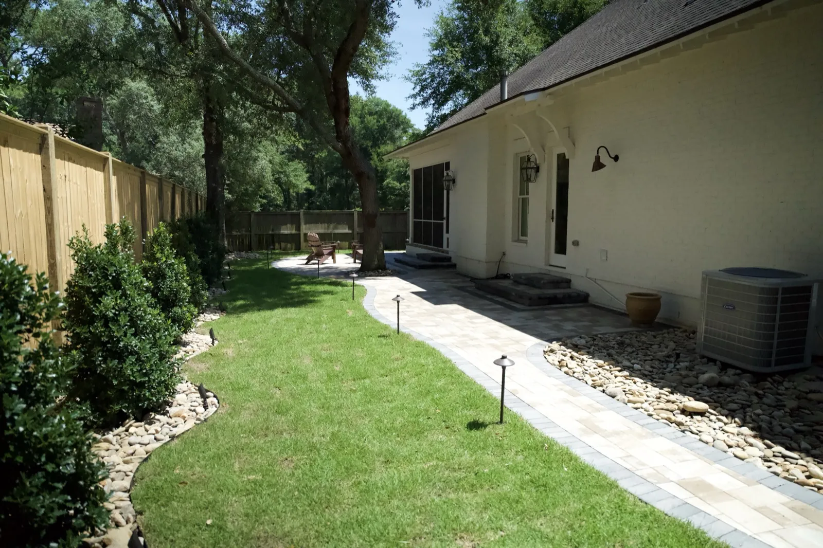 The same Point Clear backyard after the renovation — paver walkway, new sod, path lights and river-rock beds