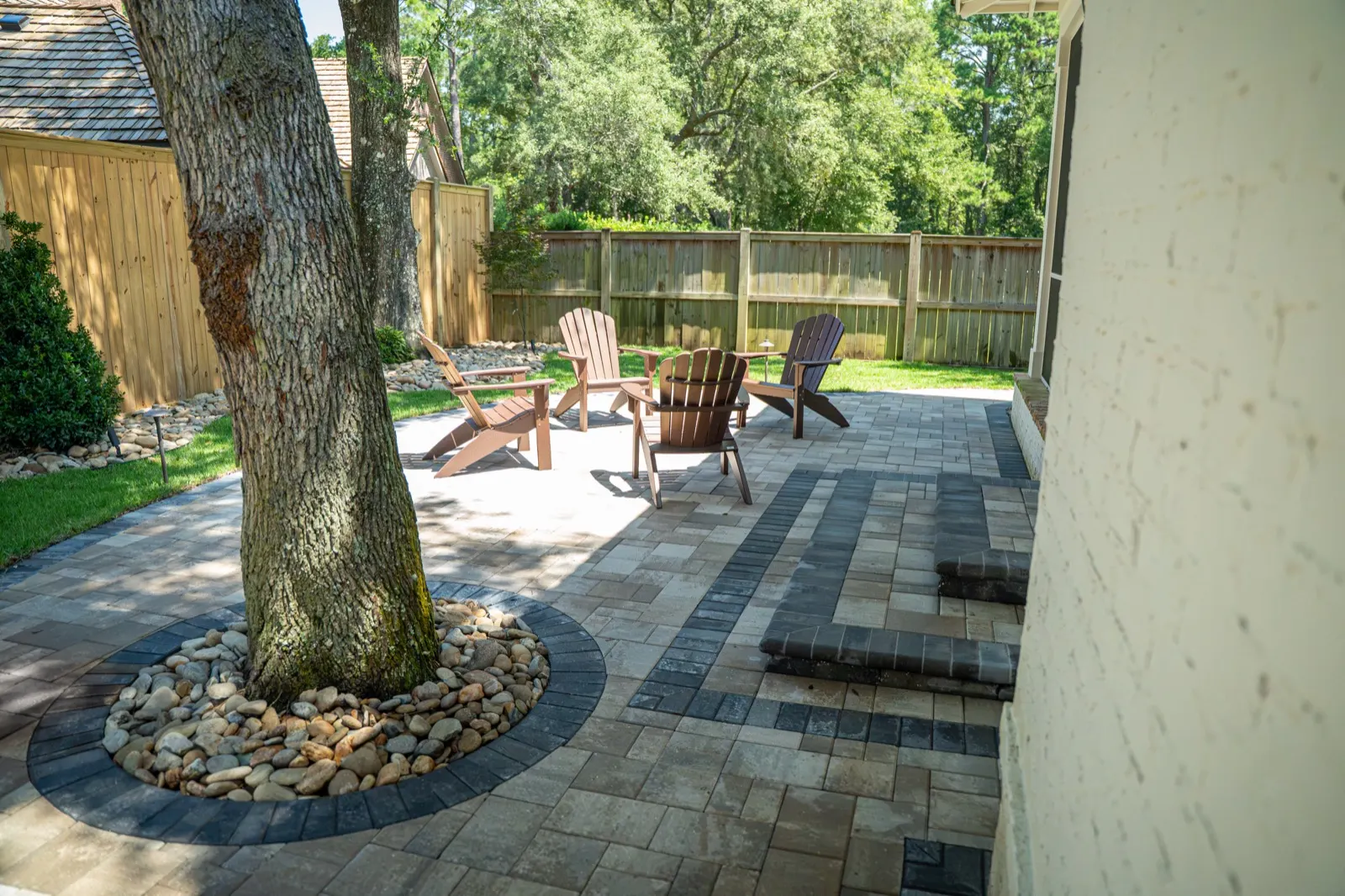 Dark paver border ringing a river rock bed around the base of a tree in a Point Clear, Alabama patio